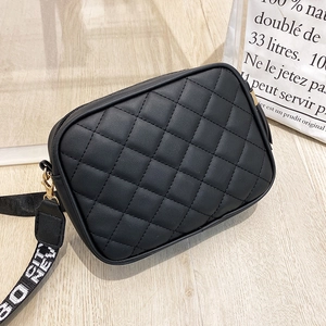 Close-up of quilted black crossbody bag featuring gold zippers and wide branded fabric strap