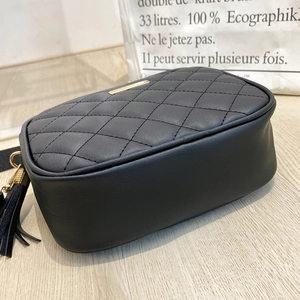 Detail view of black quilted camera bag with elegant leather tassel and gold metal hardware