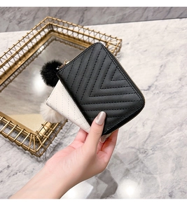 Detail of short wallets with V-quilted texture and fluffy pom-pom charms in black and white