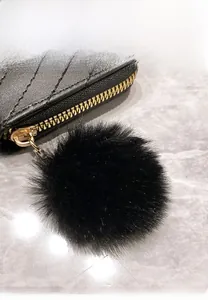 Detail of black quilted pouch featuring a soft wool ball pendant and light gold hardware