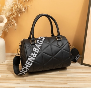 Detail einer schwarzen Stepptasche in Zylinderform mit goldenen Beschlägen und Gurt