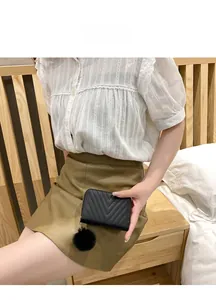 Close-up of quilted black coin purse with V-stitch patterns and fuzzy pom-pom charm