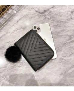 Detail of a black V-quilted mini wallet with a decorative faux fur pom-pom charm