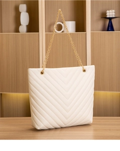 Détail d'un sac cabas blanc matelassé en V avec bandoulière chaîne dorée sur bois