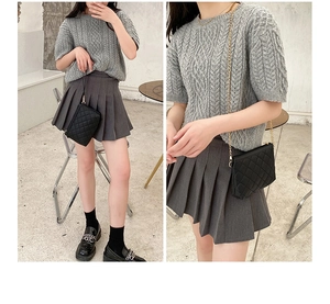 Detail of a black quilted crossbody bag styled with a grey cable knit short sleeve sweater