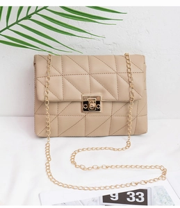 Detail of beige quilted shoulder bag with gold square lock and chain strap on light background