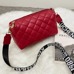 Sac bandoulière rouge matelassé avec large sangle lettrée sur un tapis moelleux