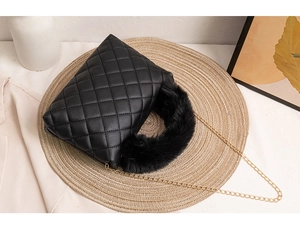 Detail of black quilted handbag with plush faux fur handle and golden chain strap