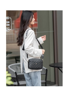 Close-up of black quilted crossbody bag with wide 'BAG' strap worn by a model