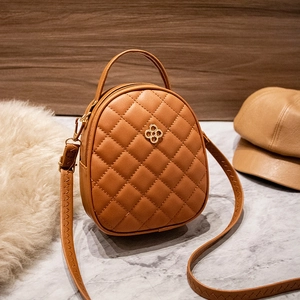 Mini sac à dos matelassé marron avec boucle trèfle dorée sur surface en marbre