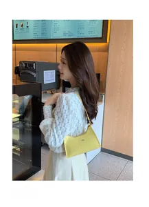 Detailed view of yellow crocodile embossed faux leather underarm bag on female model