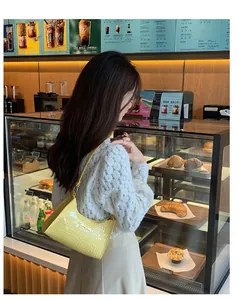 Detail of yellow crocodile embossed hobo bag with metal logo worn by a model in a cafe