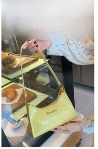 Detail of yellow crocodile embossed leather shoulder bag with metallic logo plaque