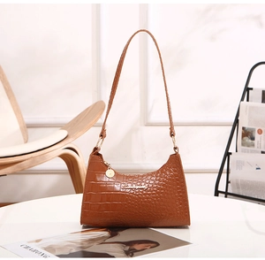 Detail of brown crocodile pattern HOBO shoulder bag with golden hardware on a table