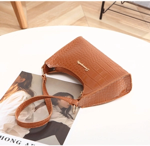 Detail of glossy brown crocodile embossed leather and golden logo on hobo handbag