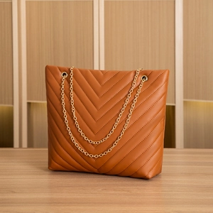 Close-up of brown V-quilted faux leather tote bag with gold chain strap on wooden surface