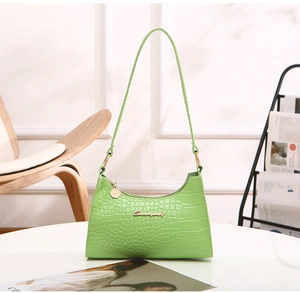 Detail of light green faux crocodile pattern and golden metal logo on the HOBO baguette bag