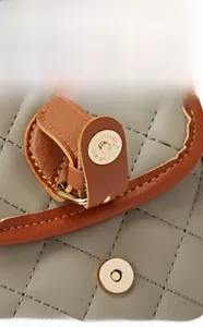 Close-up of golden magnetic snap closure on light grey quilted crossbody phone bag