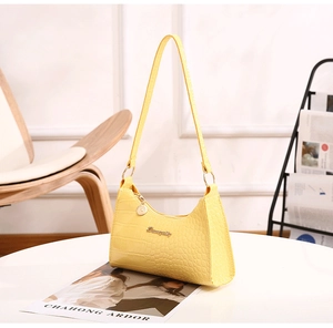 Detail of yellow crocodile pattern hobo bag with gold logo on a minimalist white table