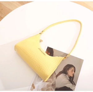 Detail shot of yellow hobo bag with crocodile texture and gold logo on white table