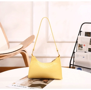 Detail of yellow crocodile embossed leather hobo bag on a minimalist white table