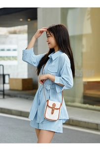 Close-up of a white quilted crossbody bag with brown trim on a blue summer outfit
