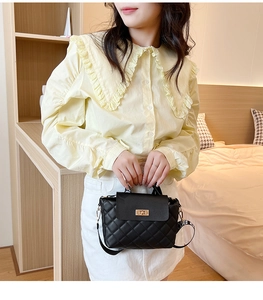 Close-up of a black quilted leather handbag with a gold twist lock on a beige outfit
