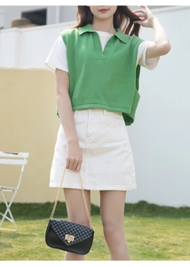 Outdoor shot of a black checkered chain bag styled with a green knit polo and white skirt