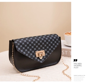 Detail of black mini crossbody phone bag with gold metal clasp and chain strap on white desk