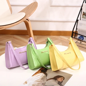 Three crocodile embossed half-moon HOBO bags in purple, green, and yellow on a white table
