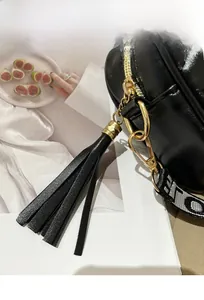 Close-up of smooth zipper with long tassel and golden metal hardware on black crossbody bag