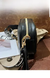 Detail of black quilted crossbody bag showing gold hardware and tassel with wide strap