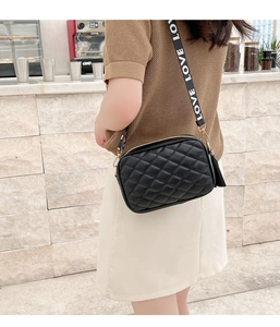 Detail of black quilted crossbody bag with golden tassel zipper and LOVE strap