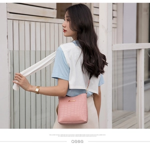 Side view of pink crocodile-embossed crossbody bag with wide strap on Asian model