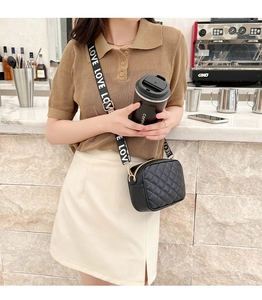 Close-up of black quilted crossbody bag with 'LOVE' printed wide strap on model