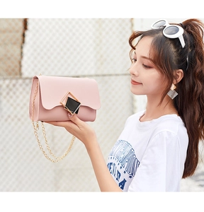 Detail shot of a soft pink leather crossbody bag with golden chain strap and buckle