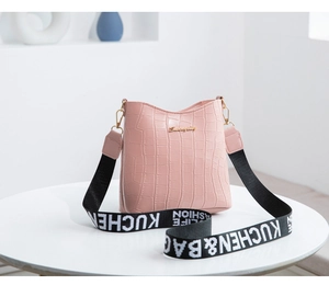 Close-up of pink crocodile texture crossbody bag with gold logo and woven shoulder strap