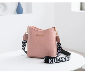 Detail of light pink crocodile pattern bucket bag with stylish wide woven shoulder strap