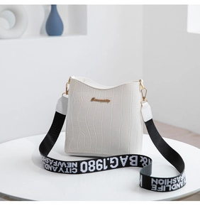 Detail of white crocodile pattern bucket bag with wide lettered strap and gold hardware