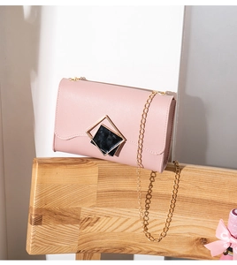 Detail of light pink crossbody bag featuring a golden geometric clasp and chain strap