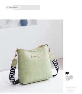 Detail view of mint green crocodile pattern bucket bag with wide woven shoulder strap