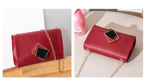 Detail view of red faux leather crossbody bag featuring a golden geometric buckle and chain