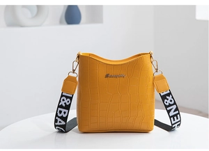 Macro view of yellow crocodile-patterned bucket bag featuring wide woven shoulder strap