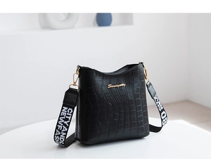 Close-up of black crocodile pattern bucket bag with golden logo and trendy woven strap