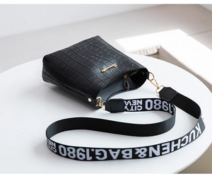 Detail of black crocodile texture bucket bag with woven wide shoulder strap and gold logo