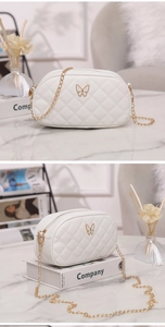 Détail du sac à bandoulière matelassé blanc avec logo papillon doré et bandoulière chaîne