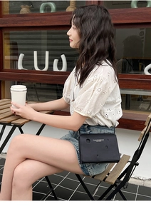 Détail du sac à bandoulière noir avec motif ajouré et lettrage blanc tendance
