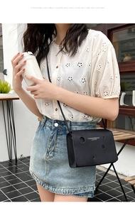 Détail du sac à bandoulière noir ajouré porté avec une tenue d'été dans un café