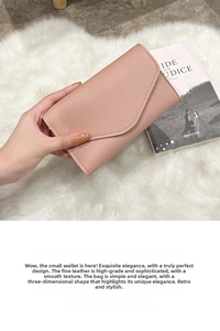 Close-up of light pink leather envelope wallet held in hand over a plush rug background