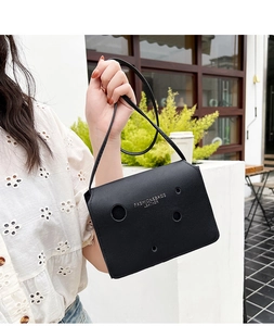 Détail du sac bandoulière en cuir noir avec découpes circulaires et texte blanc